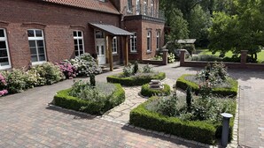 A brick building with a tiled roof, a covered entrance, and a well-maintained garden with hedges and flowers. - Hof König, apartment 4, 76 m2, 1-6 persons (Everswinkel)