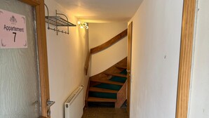 Un pasillo estrecho con una puerta de madera que indica “Apartamento 7” y que da a una escalera con alfombra verde.