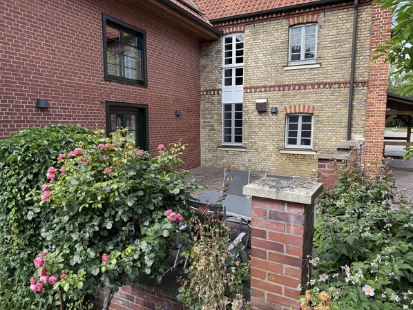 A two-story building with a brick facade, large windows, and a garden with pink flowers.