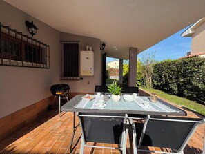 An outdoor patio with a table set for dining, a grill, and a view of a garden.