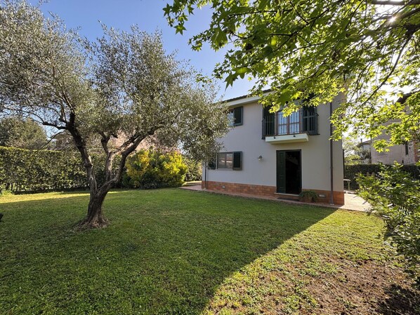 A two-story house with a well-maintained lawn, a large tree, and a balcony.