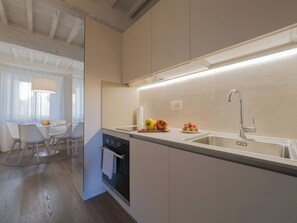 Una cocina moderna con horno empotrado, un lavamanos y una zona de comedor con mesa y sillas.