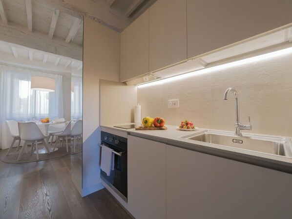 A modern kitchen with a built-in oven, a sink, and a dining area with a table and chairs.