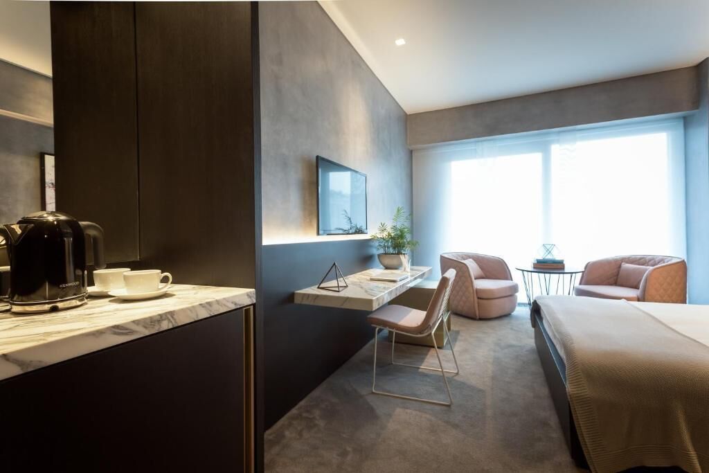 Ein modernes Hotelzimmer mit Bett, Schreibtisch, Sessel, Kaffeemaschine und Fernseher.