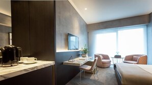Ein modernes Hotelzimmer mit Bett, Schreibtisch, Sessel, Kaffeemaschine und Fernseher.
