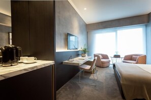 A modern hotel room with a bed, a desk, a chair, a coffee maker, and a TV.