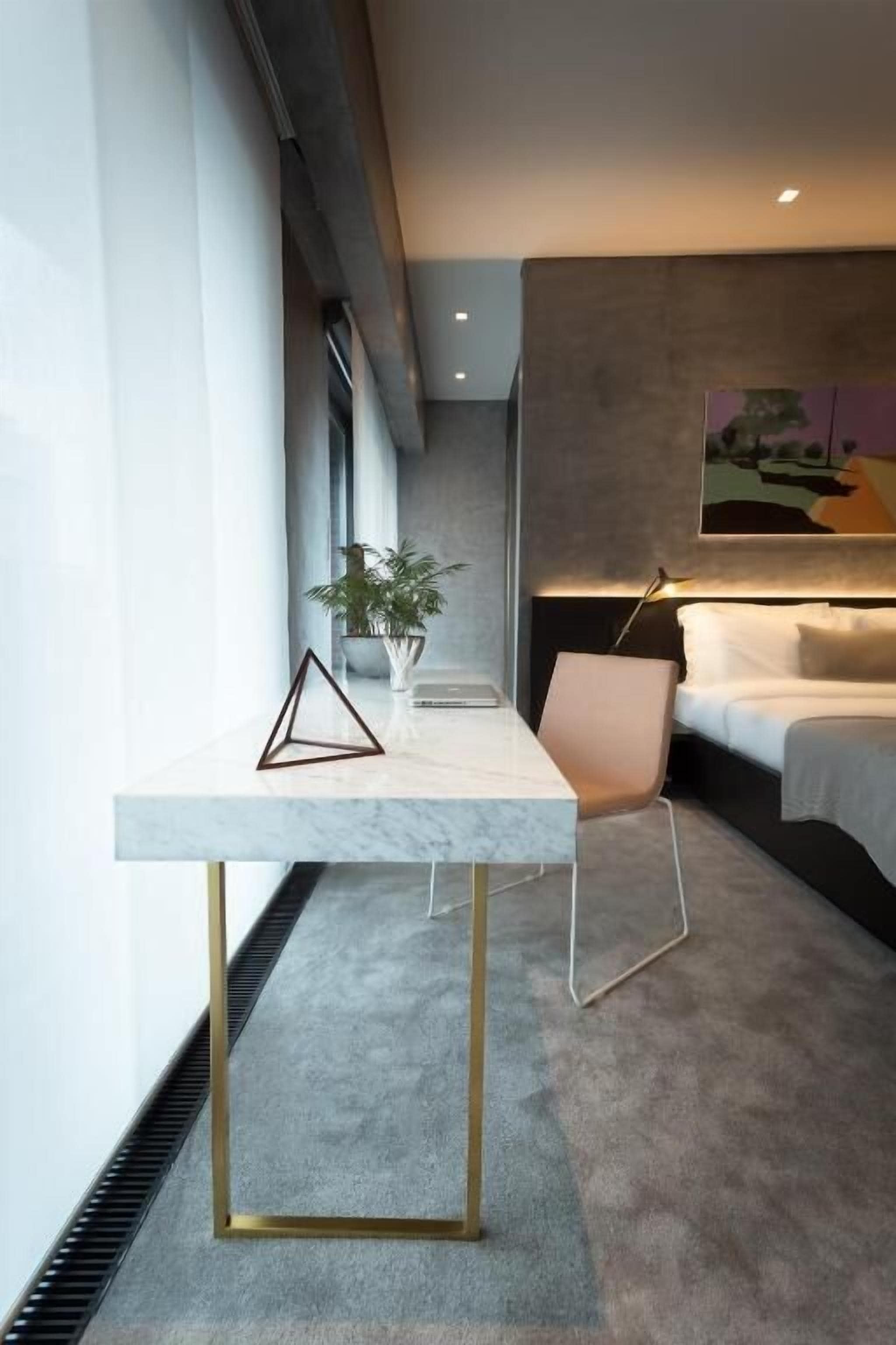 A modern bedroom with a bed, a bedside table, a chair, and a painting on the wall.