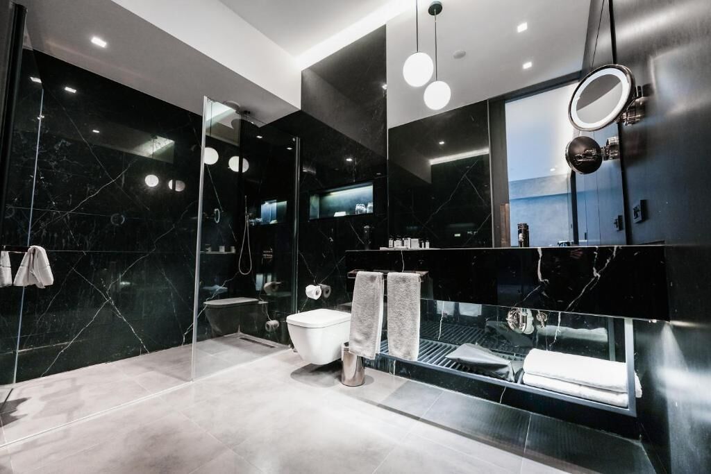Un baño moderno con ducha de vidrio, inodoro blanco y tocador negro con espejo.