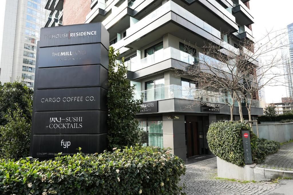 Um hotel moderno com vários andares, com uma placa indicando The House Residence, The Mill Hotel, Cargo Coffee Co. e um restaurante de sushi e cocktails.