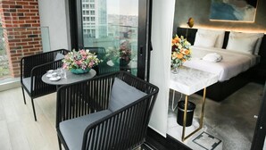 Ein Hotelzimmer mit Balkon, einem Bett, einem Tisch mit Blumenvase und Blick auf die Stadt.