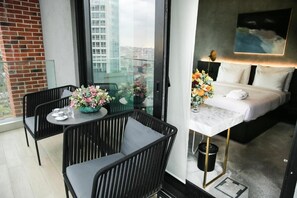 A hotel room with a balcony, a bed, a table with a vase of flowers, and a city view.