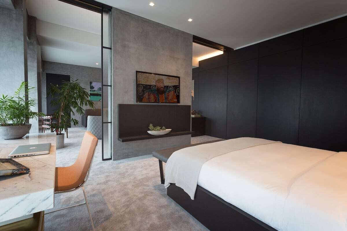 A modern bedroom with a large bed, a desk with a laptop, a chair, a potted plant, and a painting on the wall.