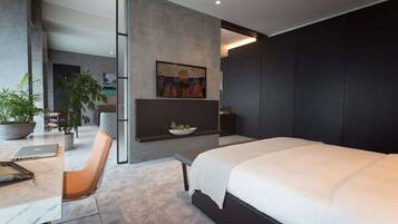 A modern bedroom with a large bed, a desk with a laptop, a chair, a potted plant, and a painting on the wall.
