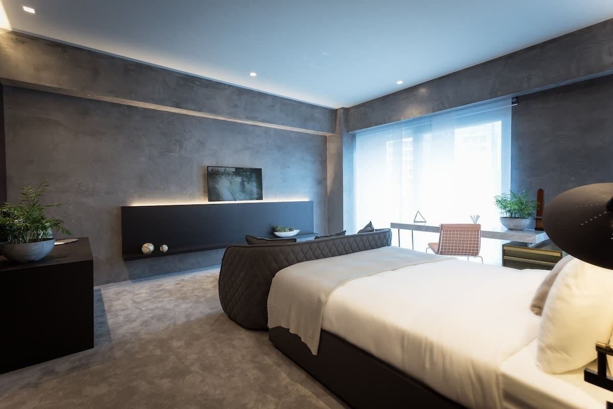 A modern bedroom with a large bed, a bedside table, a wall-mounted TV, and a window with a view.