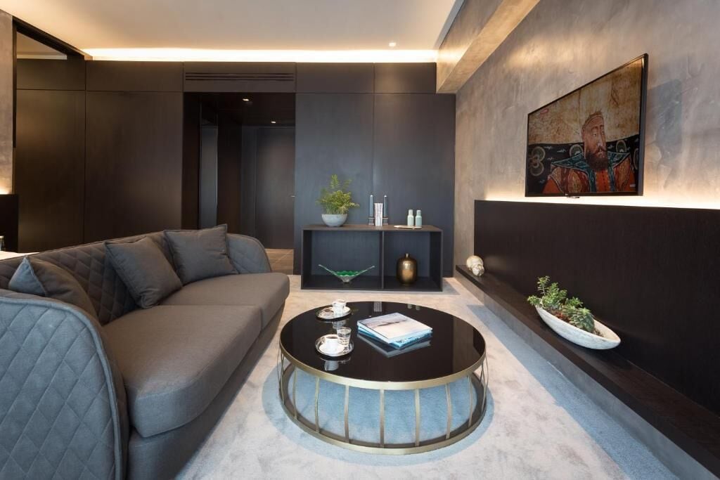 A modern living room with a grey sofa, a round coffee table, a wall-mounted TV, and a decorative shelf with plants.