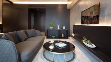 A modern living room with a grey sofa, a round coffee table, a wall-mounted TV, and a decorative shelf with plants.