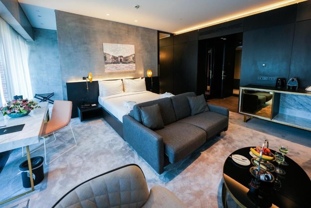 Ein modernes Hotelzimmer mit Bett, Sofa, Esstisch und einer kleinen Küchenzeile.