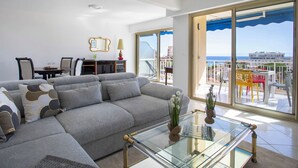 Un salon moderne avec un canapé d’angle gris, une table basse en verre et un coin repas comprenant une table et des chaises.