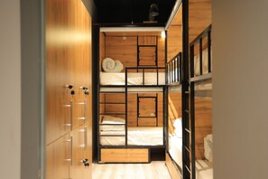 A bunk bed room with wooden walls and a ceiling light. There are two beds, one on top of the other, with pillows and blankets.