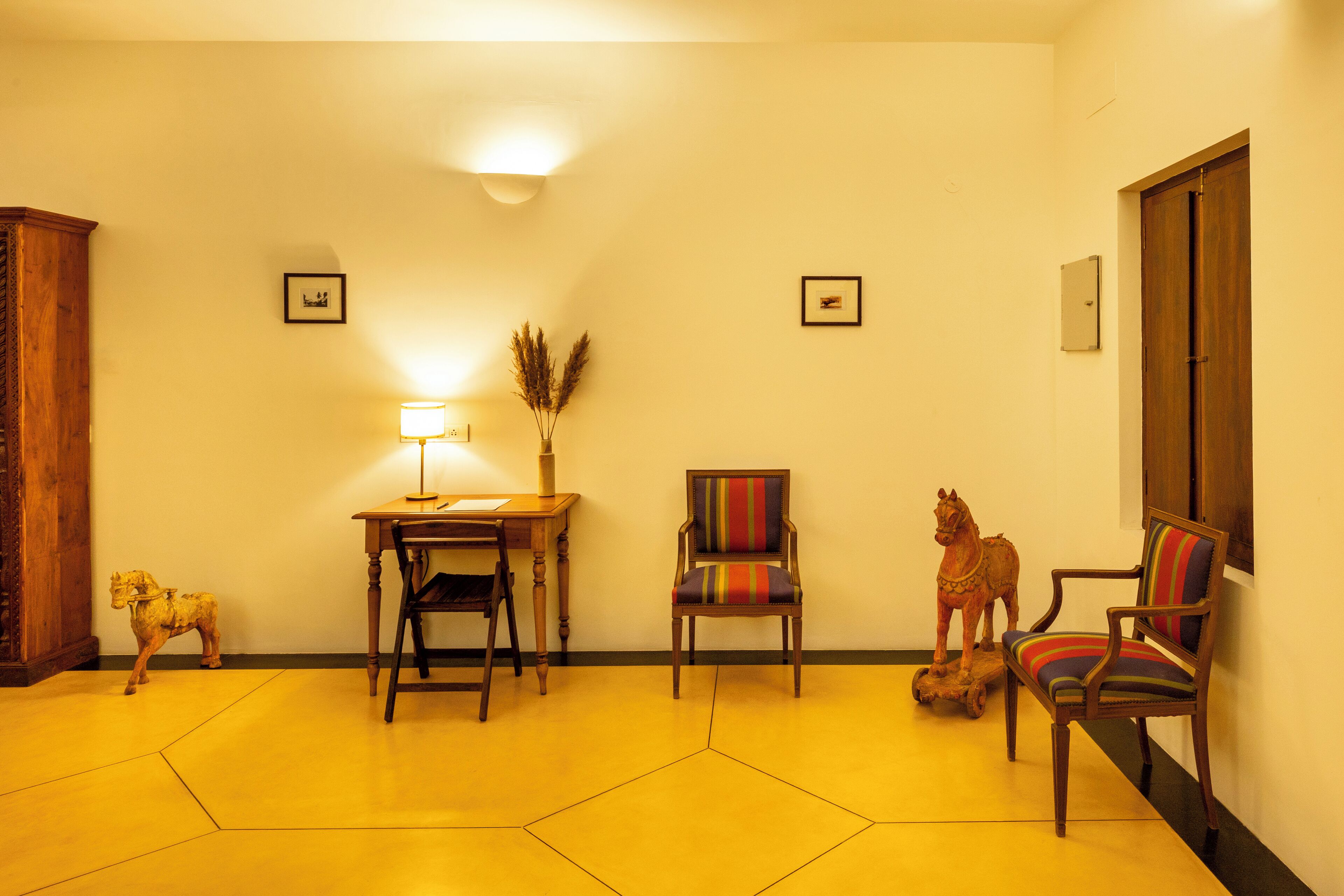 Une pièce comprenant un bureau en bois, deux chaises, une lampe et un luminaire fixé au mur.