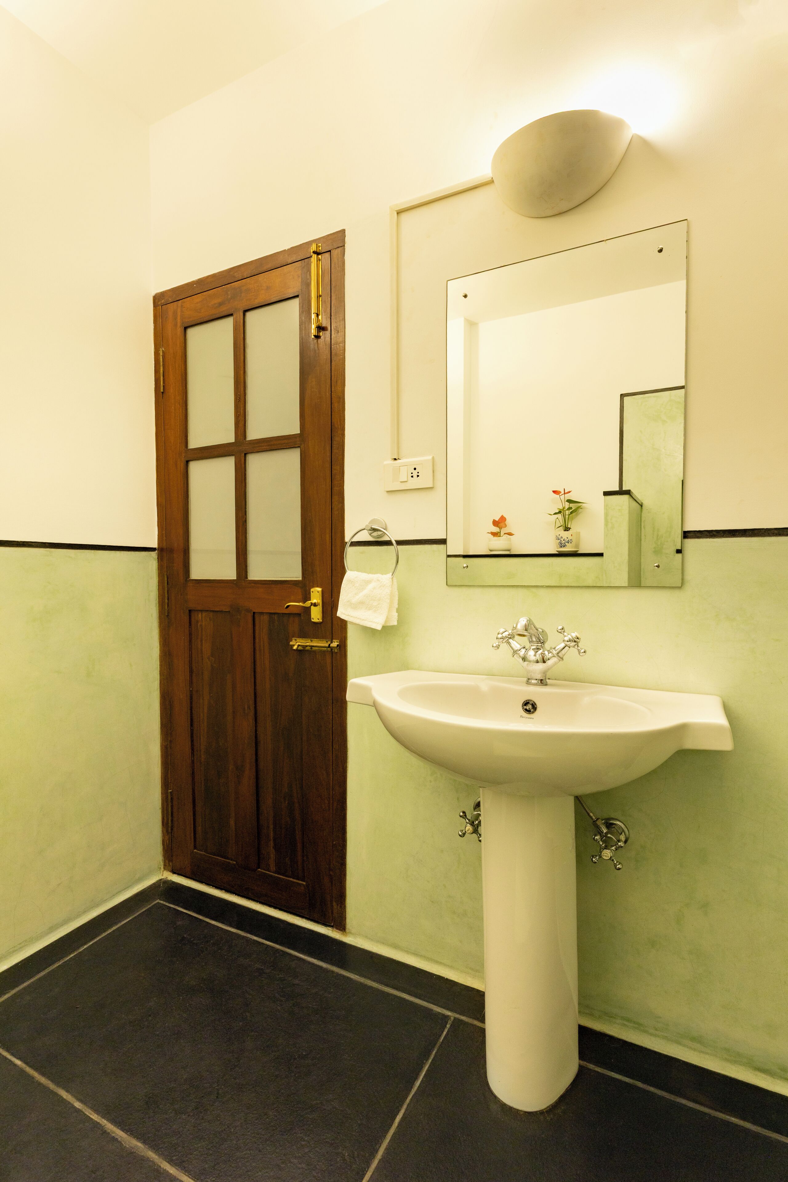 Een badkamer met een houten deur, een wit wastafeltje en een spiegel.