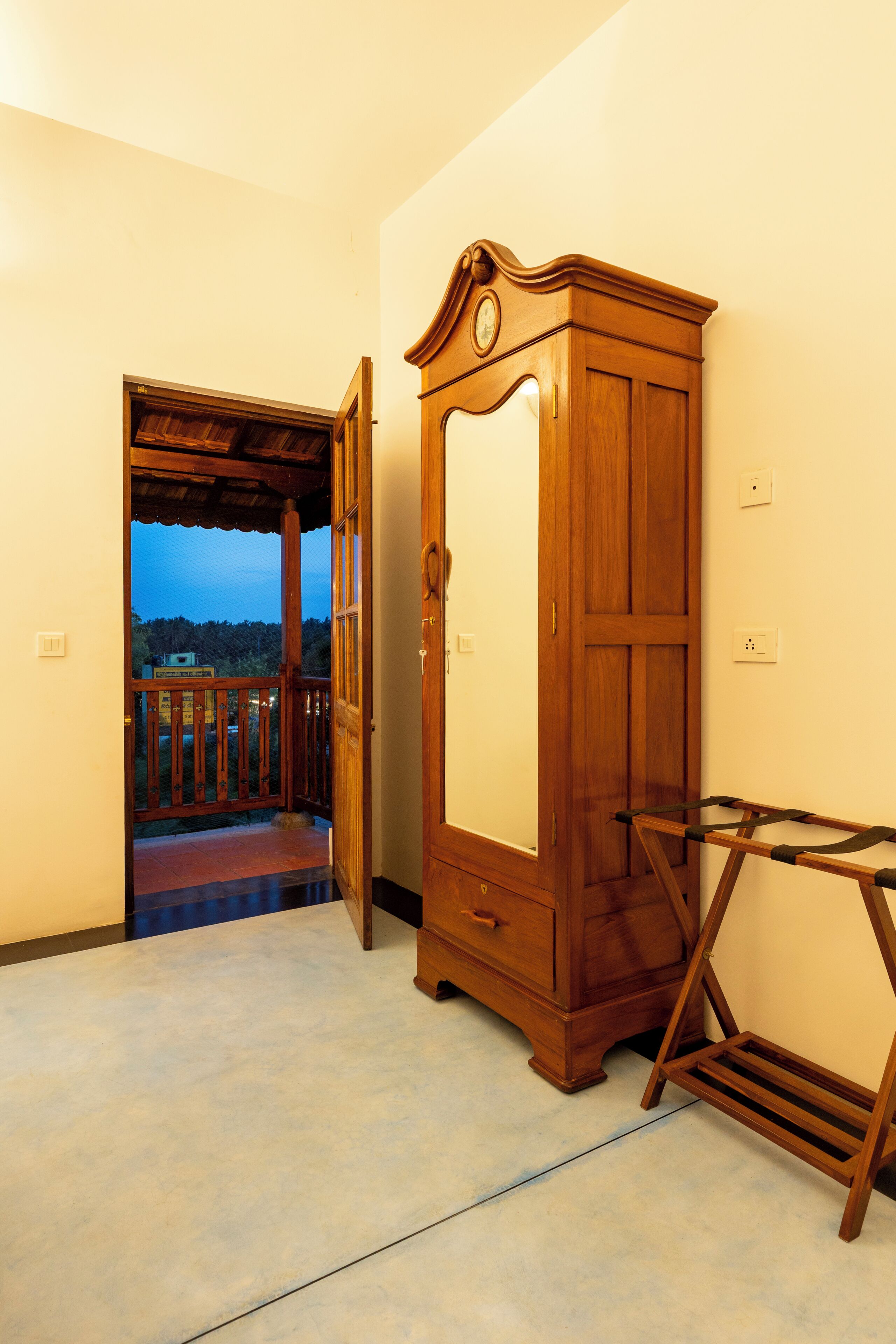 A room with a wooden wardrobe, a wooden bench, and a door leading to an outdoor balcony.