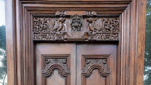 A wooden double door with intricate carvings and a coat of arms. - The Colonial Courtyard (Vanur)