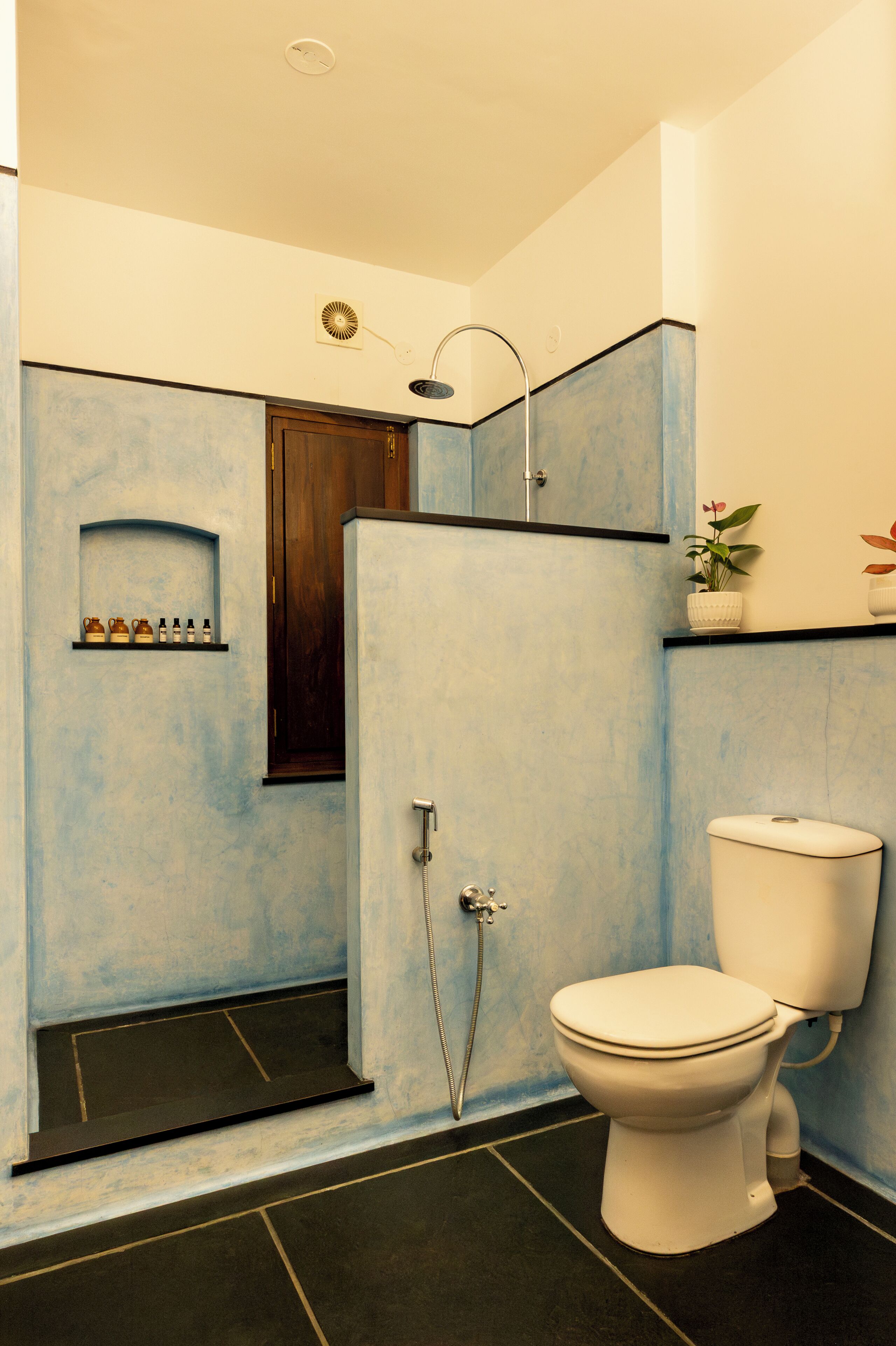 A bathroom with a shower, toilet, and a shelf with toiletries.