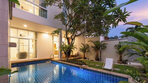 A modern pool area with a clear blue pool, surrounded by lush greenery and a well-lit outdoor seating area. - Villa Aura 3BR Private Pool Near Naiharn (Rawai)