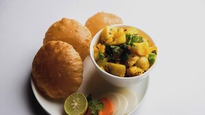 A plate with two round, golden-brown items, a bowl of yellow food with green herbs, and a slice of lime and carrot.