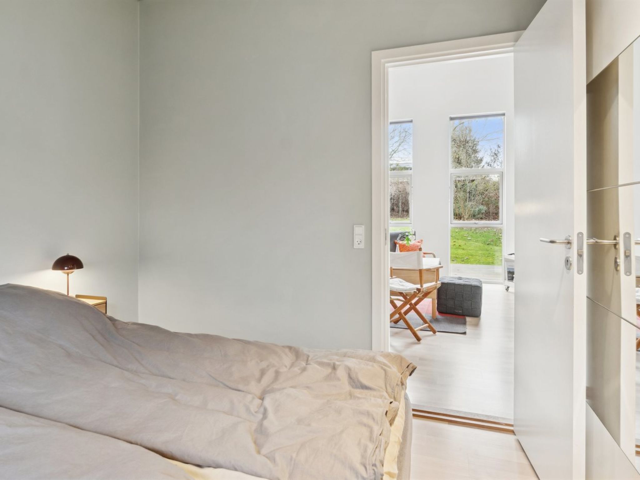 Een slaapkamer met een bed, nachtkastje en lamp. Er is een deur die leidt naar een balkon met een tafel en stoelen.