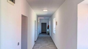 Un couloir étroit aux murs blancs et au sol gris, qui mène à une porte au fond.