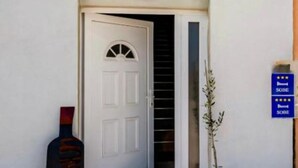 Une porte blanche avec une petite fenêtre, une enseigne bleue avec le mot « SOBE » et des étoiles, et une plante placée à côté de la porte.