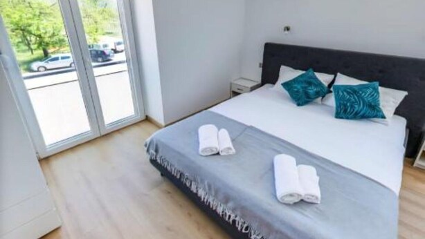 A modern hotel room with a large bed, two pillows, and a view of the street through a sliding door. - Rooms Burnum - Double Room 3 (Vrbnik-Knin)
