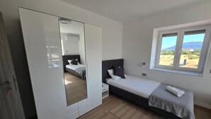 A bedroom with a bed, a wardrobe, a window with a view, and a mirror. - Rooms Burnum - Twin Room 7 (Vrbnik-Knin)