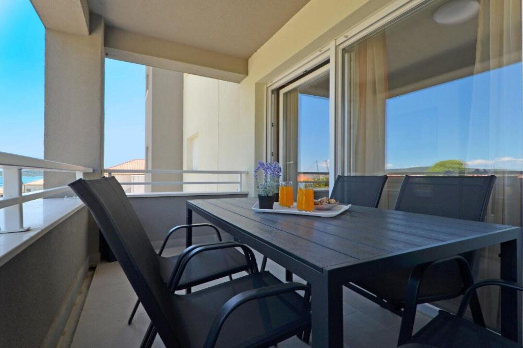 Ein Balkon mit Tisch, Stühlen, einem Blumentopf und einer Serviertablett mit Getränken.