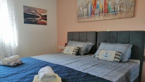A double bed with a blue quilt, two pillows with anchor designs, and rolled towels on the bed.