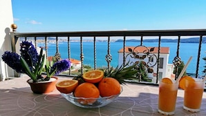 A balcony with a clear view of the sea, a bowl of oranges, and two drinks.