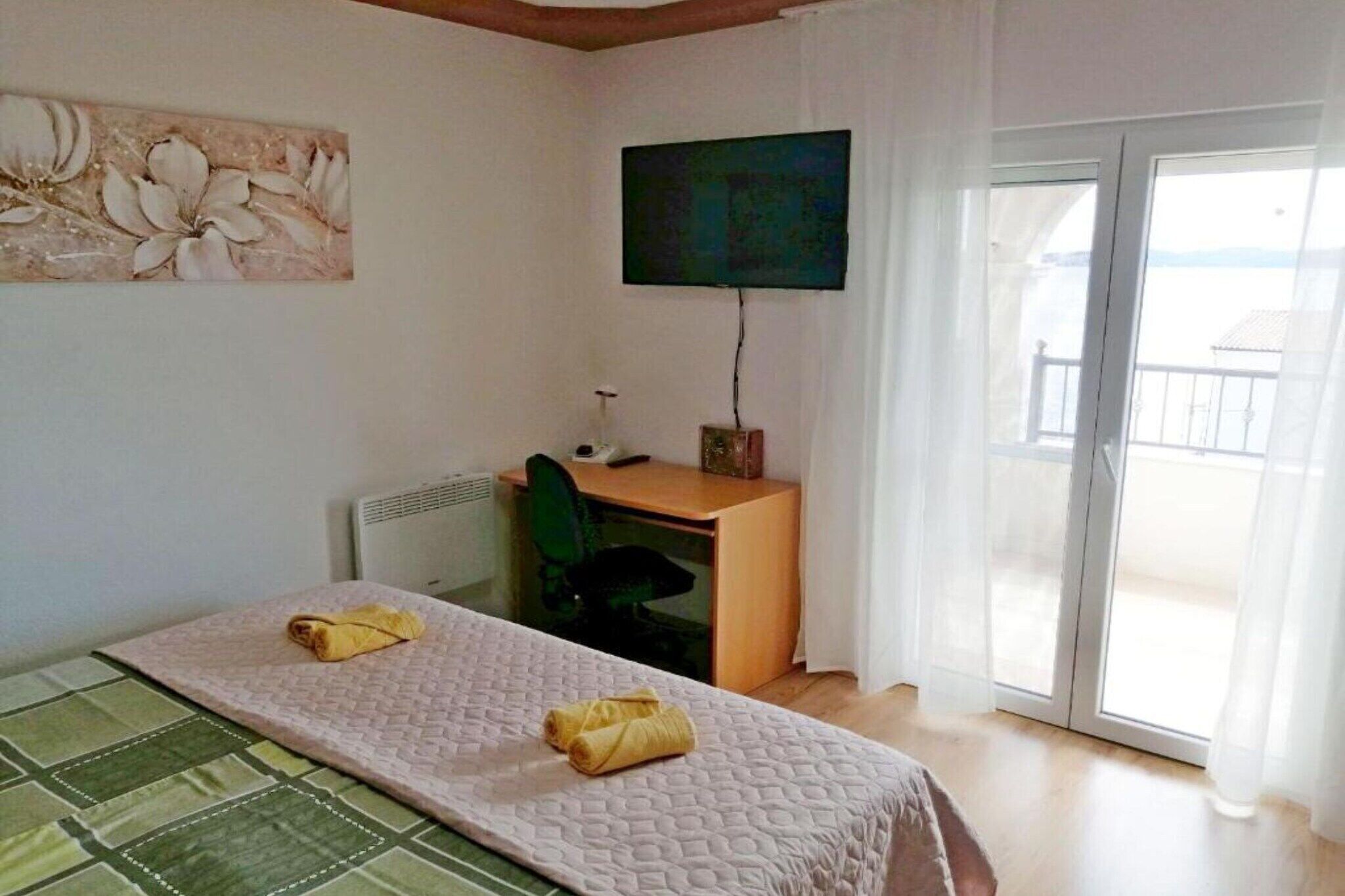 A room with a bed, a desk, a chair, a television, and a sliding glass door to the outside.