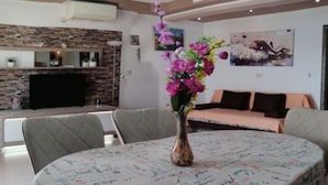 A modern living room with a stone fireplace, a dining table with a floral centerpiece, and a sofa with cushions.
