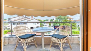 Un balcon avec deux fauteuils en osier et une petite table ronde, le tout recouvert d’une auvent de couleur beige.