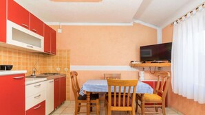 Une cuisine de taille réduite avec des meubles de rangement rouges, une table à manger avec des chaises et un téléviseur posé sur un meuble.