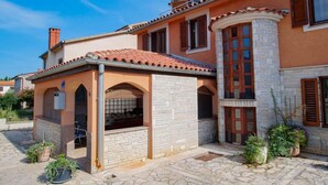 Un bâtiment de style méditerranéen, doté d’une façade en pierre, d’un toit en tuiles et d’un petit patio couvert agrémenté de plantes en pot.