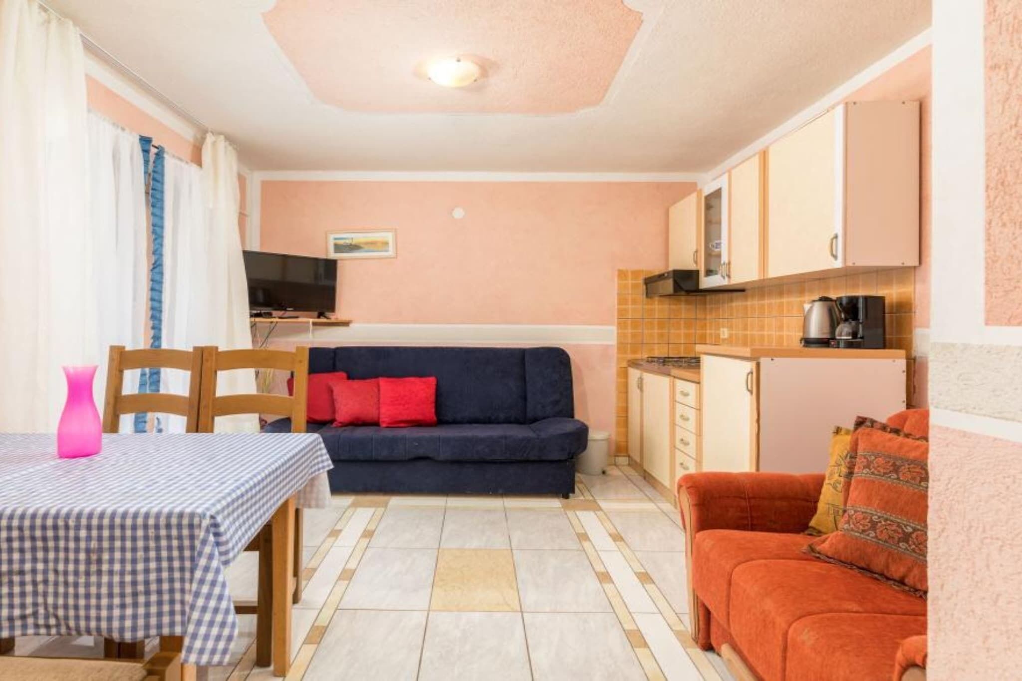 Un espacio habitable compacto con sofá, una mesa de comedor con mantel a cuadros, televisor y alacenas de cocina.