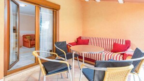 Un espace extérieur accueillant avec un canapé et des fauteuils à rayures, une porte vitrée donnant sur un balcon et un sol carrelé.