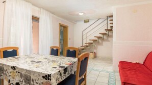 Un comedor con una mesa cubierta por un mantel floral, rodeada de sillas de madera. Un sofá rojo es visible al frente.