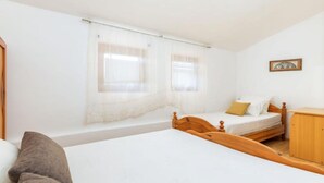 Un dormitorio con dos camas, cabeceros de madera, un armario de madera y una ventana con cortinas traslúcidas.