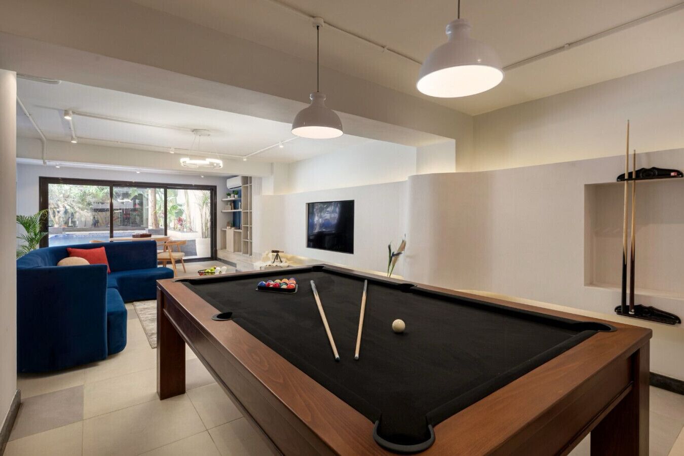 A modern living room with a pool table, a blue sofa, and a television mounted on the wall.