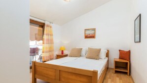 Quarto com cama de madeira, mesa de cabeceira com abajur, uma mesinha, uma cadeira e um quadro na parede.