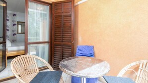 Quarto com porta de vidro que dá para uma varanda, mesa redonda com uma cadeira e toalha azul no chão.